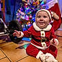 Maylon a rejoint le concours — aidez-le/la à gagner de superbes lots ! baby, infant, toddler, christmas, christmas_tree, santa_costume, red_costume, santa_hat, smile, happy, sitting, tile_floor, stroller_wheel, ornaments, bokeh, festive, decoration, portrait, cozy, holiday