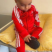 Ilyes participe au concours pour gagner de l'argent avec cette photo : toddler, child, red_tracksuit, sneakers, yellow_cushion, indoor, drawer, household_items, black_shoes, sitting, curious, baby, clothing, footwear, person, casual, young_child, wall, table, home
