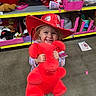 Astrid is registered to the contest to win money with this photo: toddler, child, plush_toy, red_hat, toy_store, smile, happy, stuffed_animal, floor, shelf, packaging, colorful, indoor, person, clothing, cute, holding, playful, young_child, hat