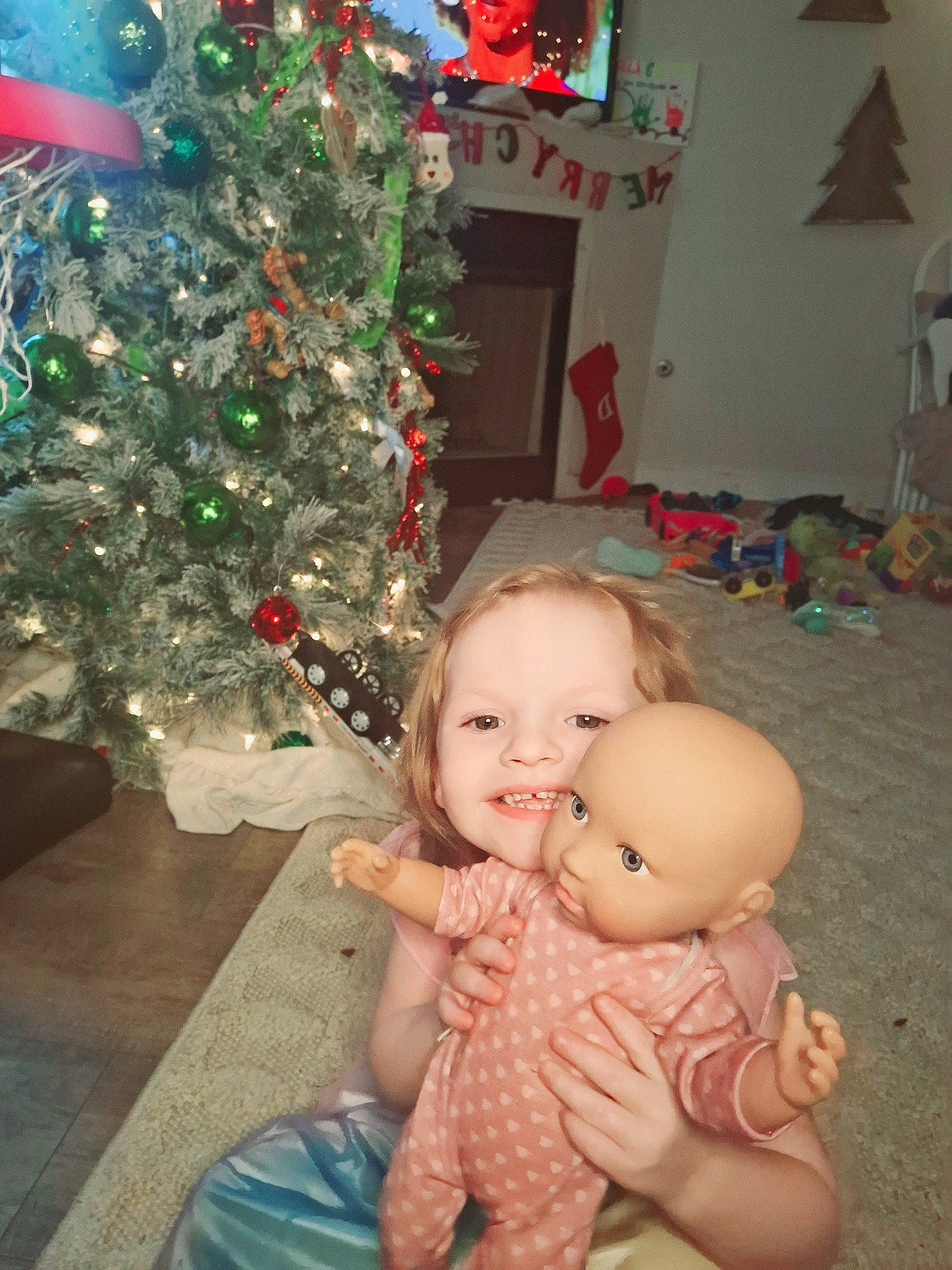 Charli is registered to the contest to win money with this photo: cheek, christmas_decoration, christmas_ornament, christmas_tree, event, facial_expression, fun, happy, holiday, holiday_ornament, human_body, lap, mammal, people, person, photograph, smile, snapshot, standing, toddler