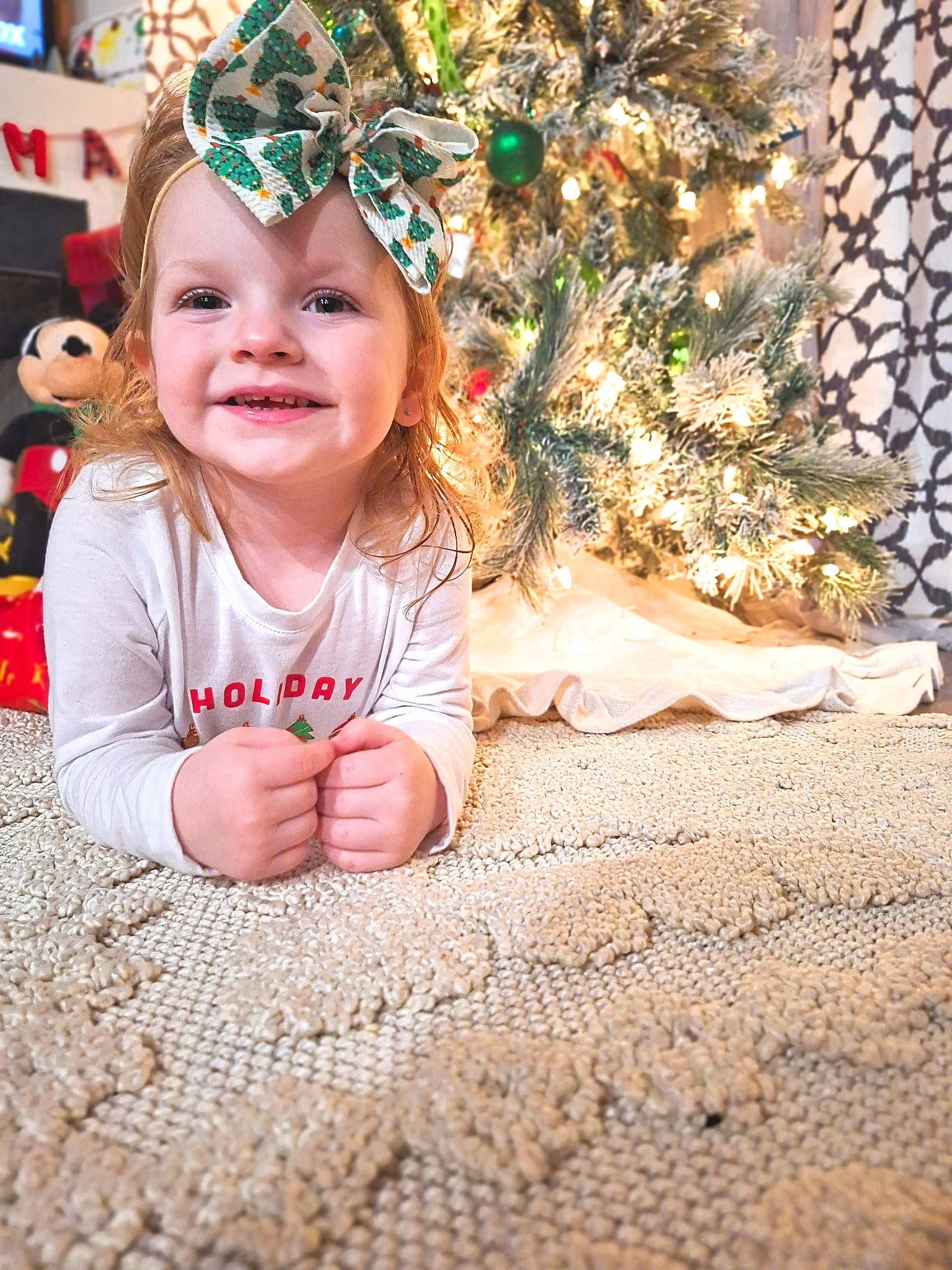 Charli is registered to the contest to win money with this photo: baby, baby_toddler_clothing, child, christmas_decoration, christmas_ornament, christmas_tree, event, facial_expression, flooring, foot, fun, grass, happy, headwear, joy, leaf, people_in_nature, person, plant, smile