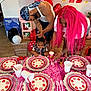 child, birthday_party, toddler, pink_hair, balloons, table_setting, strawberry_theme, plates, plastic_cups, cutlery, adults, celebration, decorations, indoor, people, festive, high_chair_box, wood_floor, curly_hair, party