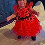 Heaven joined the competition — help win amazing prizes! black_shoes, black_spots, blurred_person, child, costume, curly_hair, decorations, flooring, fun, halloween, headband, indoor, ladybug_costume, party, person, red_dress, smile, table, toddler, wooden_floor