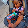 toddler, child, car_seat, bow, sippy_cup, pink_nail_polish, indoors, kitchen, tile_floor, straps, bracelet, clothing, person, baby, cute, hair, seatbelt, hand, foot, floor
