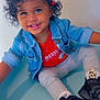 black_sneakers, casual, child, curly_hair, cute, denim_jacket, fashion, hair_clips, happy, indoor, leggings, person, playful, portrait, red_shirt, sitting, smiling, studio, toddler, young_child