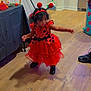 antenna, black_shoes, broom, celebration, child, costume, curly_hair, cute, decorations, halloween, headband, indoor, ladybug, party, person, red_dress, table, toddler, wooden_floor, young_child