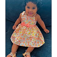 Heaven is registered to the contest to win money with this photo: toddler, child, smiling, curly_hair, floral_dress, bow, sitting, couch, sandals, happy, cute, indoor, portrait, baby, face, young_child, fashion, playful, comfortable, casual