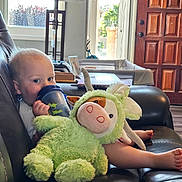 Ronan is registered to the contest to win money with this photo: baby, child, sippy_cup, stuffed_animal, plush_toy, couch, leather, living_room, lamp, window, door, foot, hand, toy, indoor, person, cute, relaxing, furniture, home