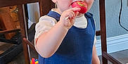 Ronan is registered to the contest to win money with this photo: toddler, child, lollipop, blue_outfit, indoor, carpet, toy, television, table, wooden_furniture, curious, standing, home, play_area, cute, baby, face, hand, room, floor