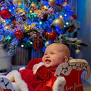 Daphne is registered to the contest to win money with this photo: baby, child, christmas_tree, ornaments, lights, holiday, sleigh, red_clothing, smiling, festive, indoor, decorations, happy, face, celebration, winter, cute, seasonal, christmas, infant