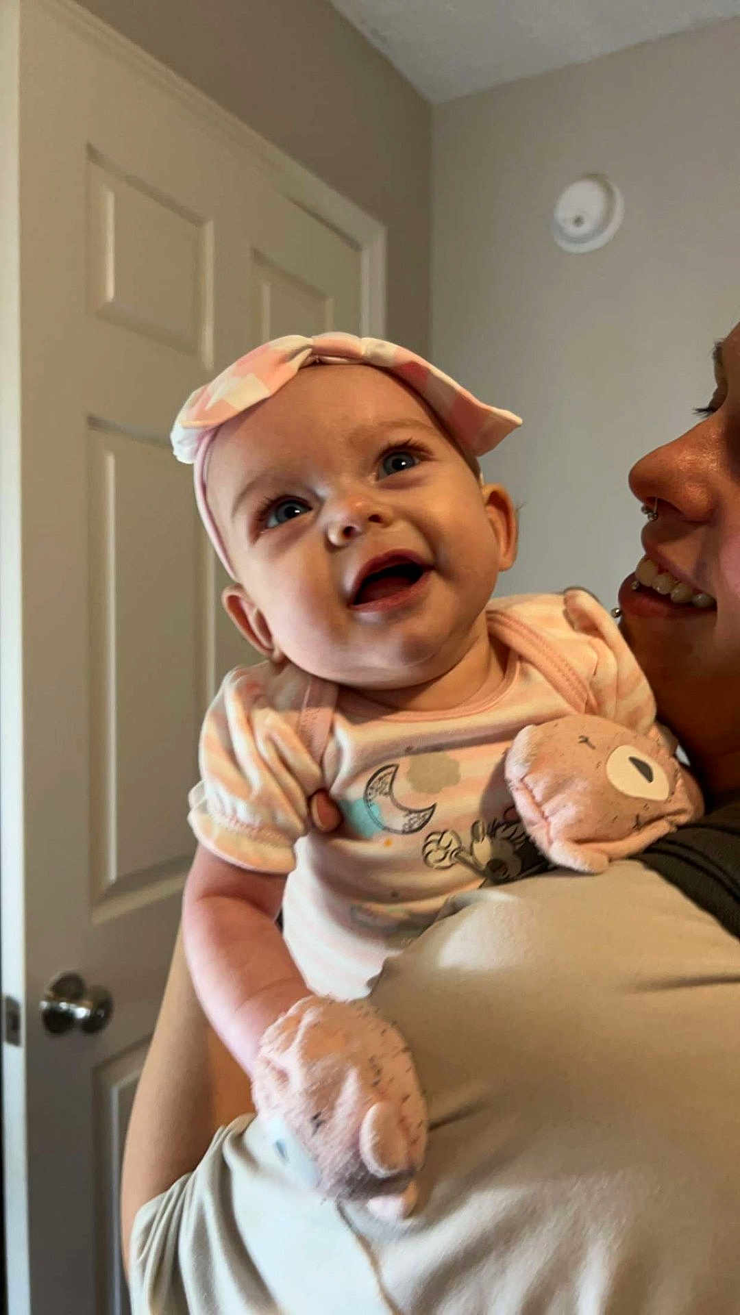 Octavia is registered to the contest to win money with this photo: baby, infant, smiling, headband, mittens, adult, person, indoor, door, clothing, holding, cute, happy, face, portrait, closeup, child, expression, parent, love