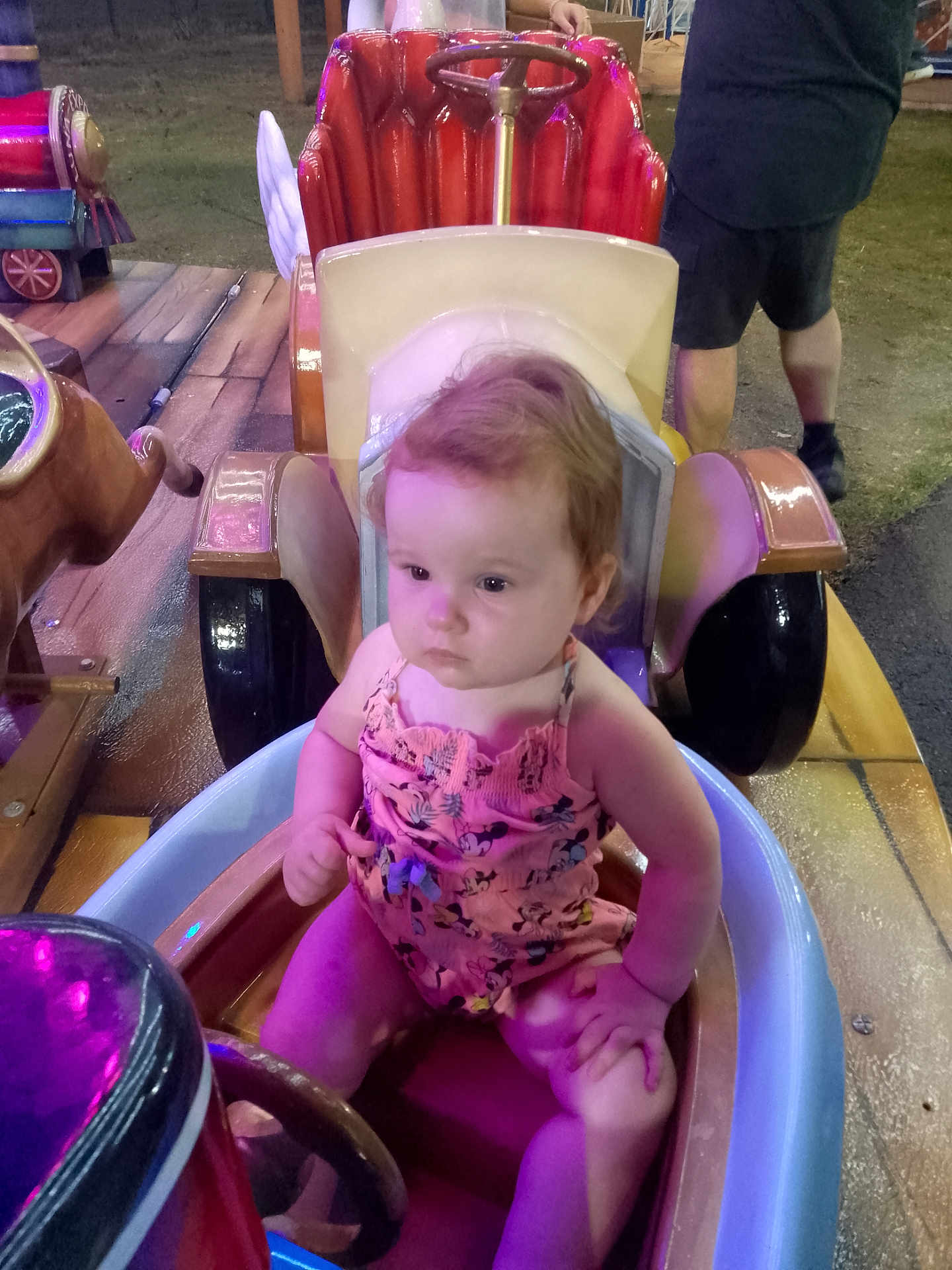 Cassidy participe au concours pour gagner de l'argent avec cette photo : adult, amusement_ride, child, colorful, face, fairground, hair, hands, night, outdoor, person, pink_clothing, play, purple_light, ride_car, seat, shorts, steering_wheel, toddler, toy_car