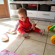 Cassidy a rejoint le concours — aidez-le/la à gagner de superbes lots ! baby, cabinet, child, door, floor, footwear, furniture, indoor, leggings, living_room, pink, play, red_dress, slippers, smile, sunlight, television, tile, toddler, toy