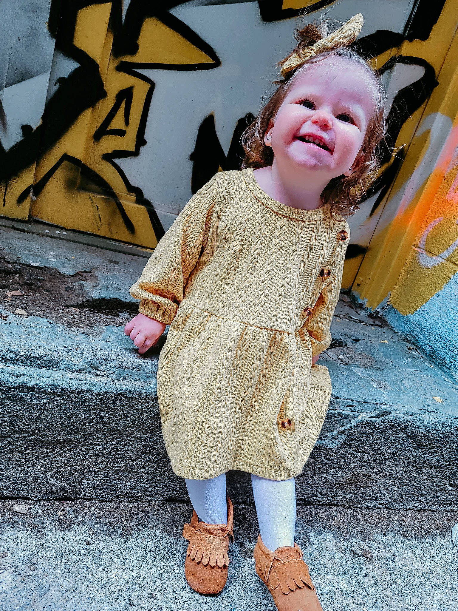 Anastyn is registered to the contest to win money with this photo: asphalt, blond, child, fashion_accessory, flooring, fun, hairstyle, happy, head, human_leg, leisure, pattern, person, skin, sleeve, smile, standing, street_fashion, textile, toddler