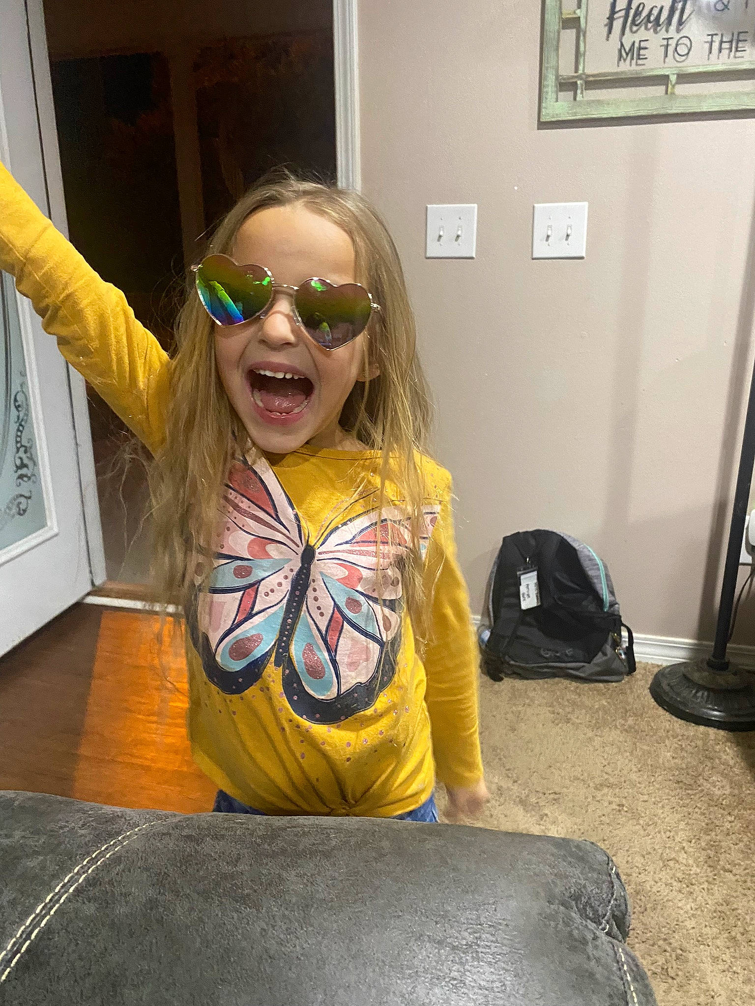 Amiya is registered to the contest to win money with this photo: bag, blond, child, cool, eyewear, facial_expression, floor, flooring, fun, goggles, happy, luggage_and_bags, person, personal_protective_equipment, sitting, smile, sunglasses, t_shirt, toddler, vision_care