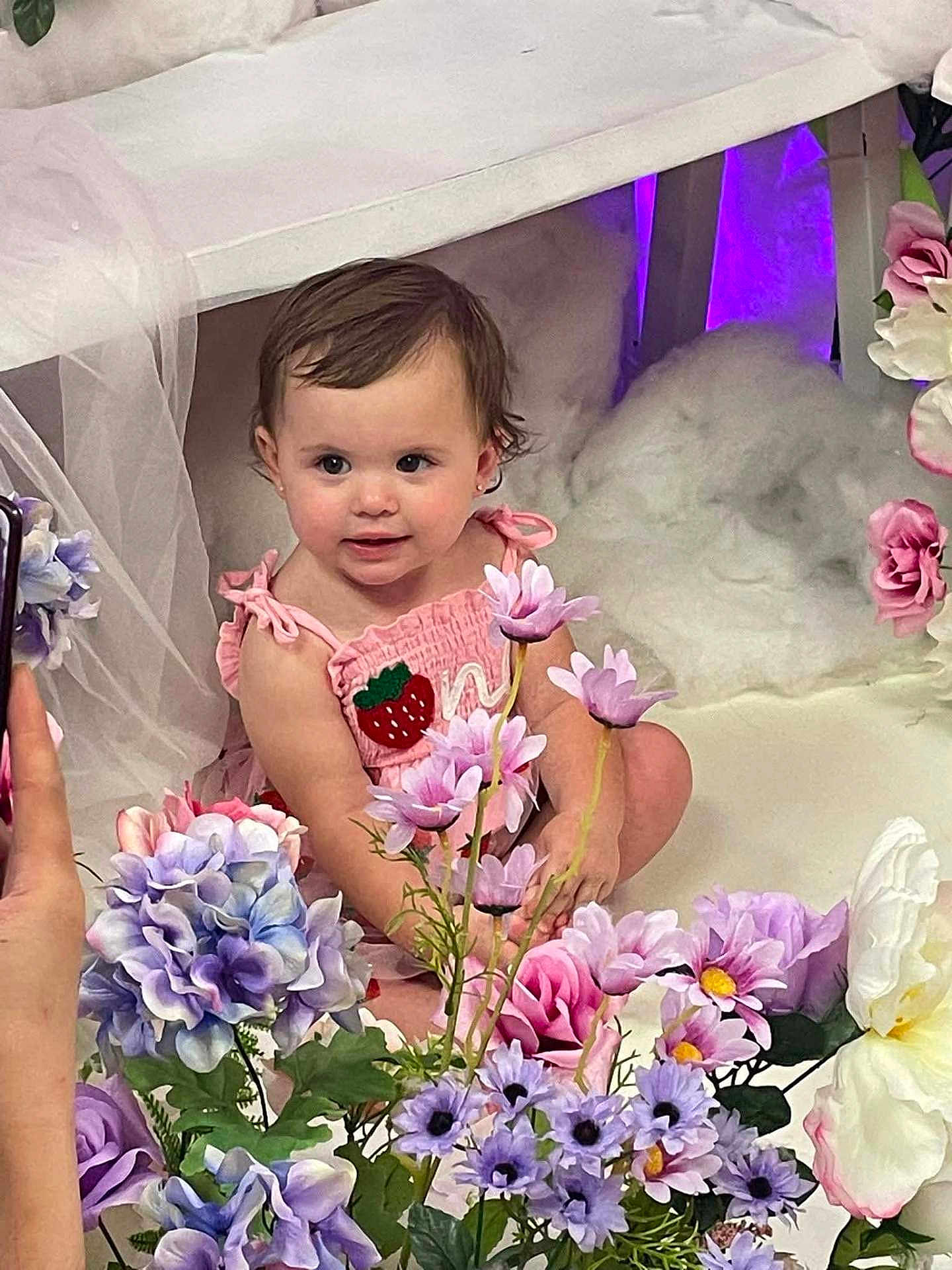 Vyolette is registered to the contest to win money with this photo: baby, child, cute, decor, flower_arrangement, hand, human, indoor, person, phone, photography, pink_dress, pink_flowers, portrait, purple_flowers, sitting, smiling, strawberry_patch, toddler, white_flowers