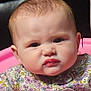 baby, child, face, expression, pink, chair, clothing, floral_pattern, portrait, cute, indoor, young_child, person, head, skin, hair, eyebrows, lips, serious_expression, closeup