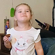 Taelynn joined the competition — help win amazing prizes! braided_hair, candid_photo, casual_clothing, cat_shirt, child, cup, face, girl, hand, holding_food, indoor, little_girl, living_room, person, photo_on_cup, portrait, smartphone, snack, sofa, toddler