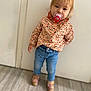 blond_hair, casual_wear, child, curious, door, expression, floor, home, indoor, jeans, pacifier, patterned_clothing, person, portrait, shirt, shoes, standing, toddler, wooden_floor, young_child