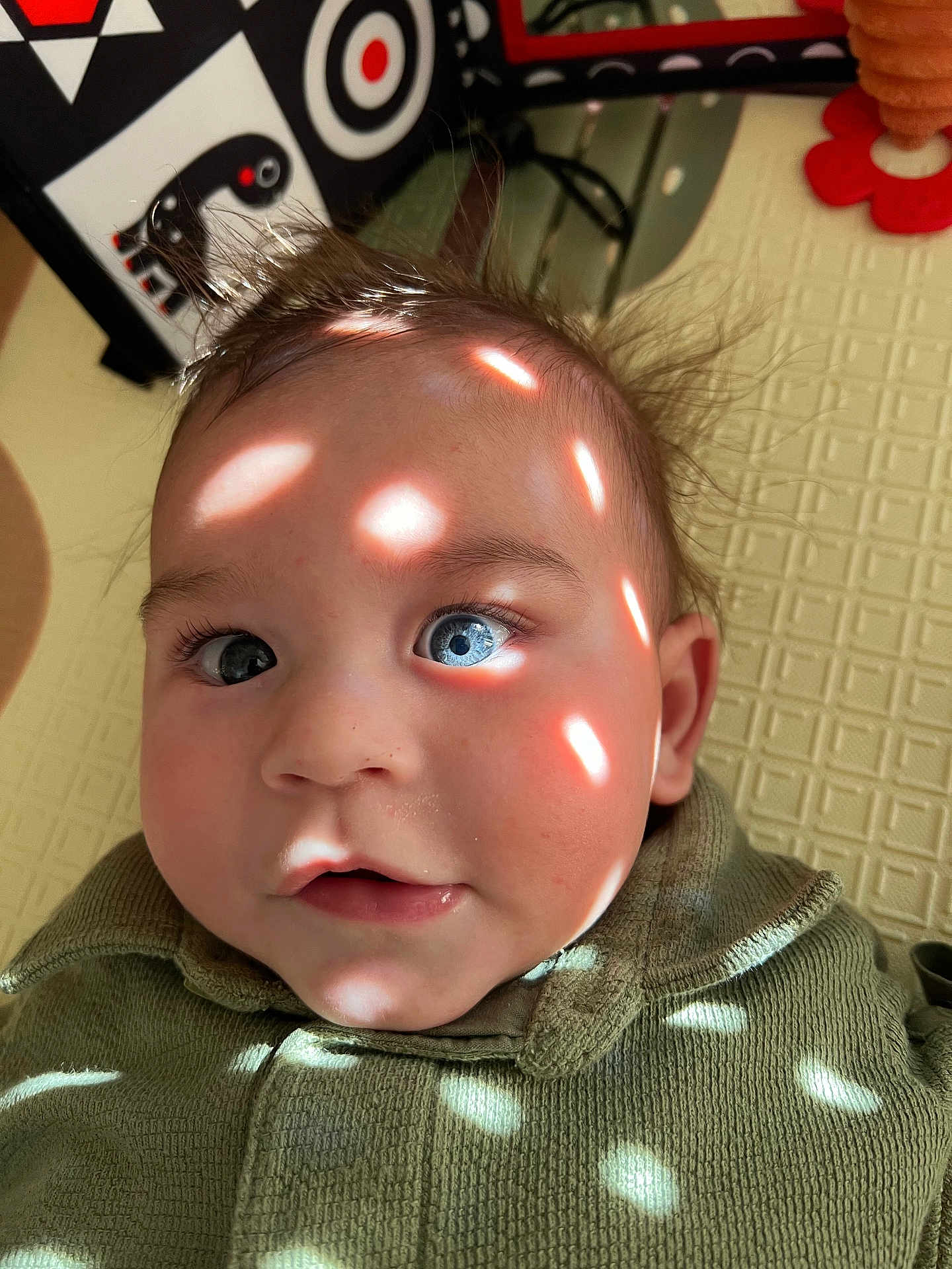 Camille participe au concours pour gagner de l'argent avec cette photo : baby, blue_eyes, close_up, face, light_spots, infant, indoors, playmat, texture, green_clothing, cute, expression, child, portrait, soft_light, hair, toy, pattern, skin, young
