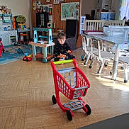 Milan a rejoint le concours — aidez-le/la à gagner de superbes lots ! toddler, child, toy_shopping_cart, playroom, toys, floor, table, chairs, window, natural_light, kitchen_toy, rug, plastic_toys, indoor, wooden_furniture, colorful, curtains, storage_box, floor_tiles, person