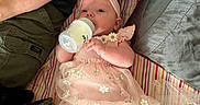 Hannah joined the competition — help win amazing prizes! baby, infant, bottle, feeding, pink_dress, headband, flower_pattern, striped_blanket, adult_arm, casual_clothing, relaxation, indoor, lying_down, cute, child, person, soft_texture, comfort, family, moments
