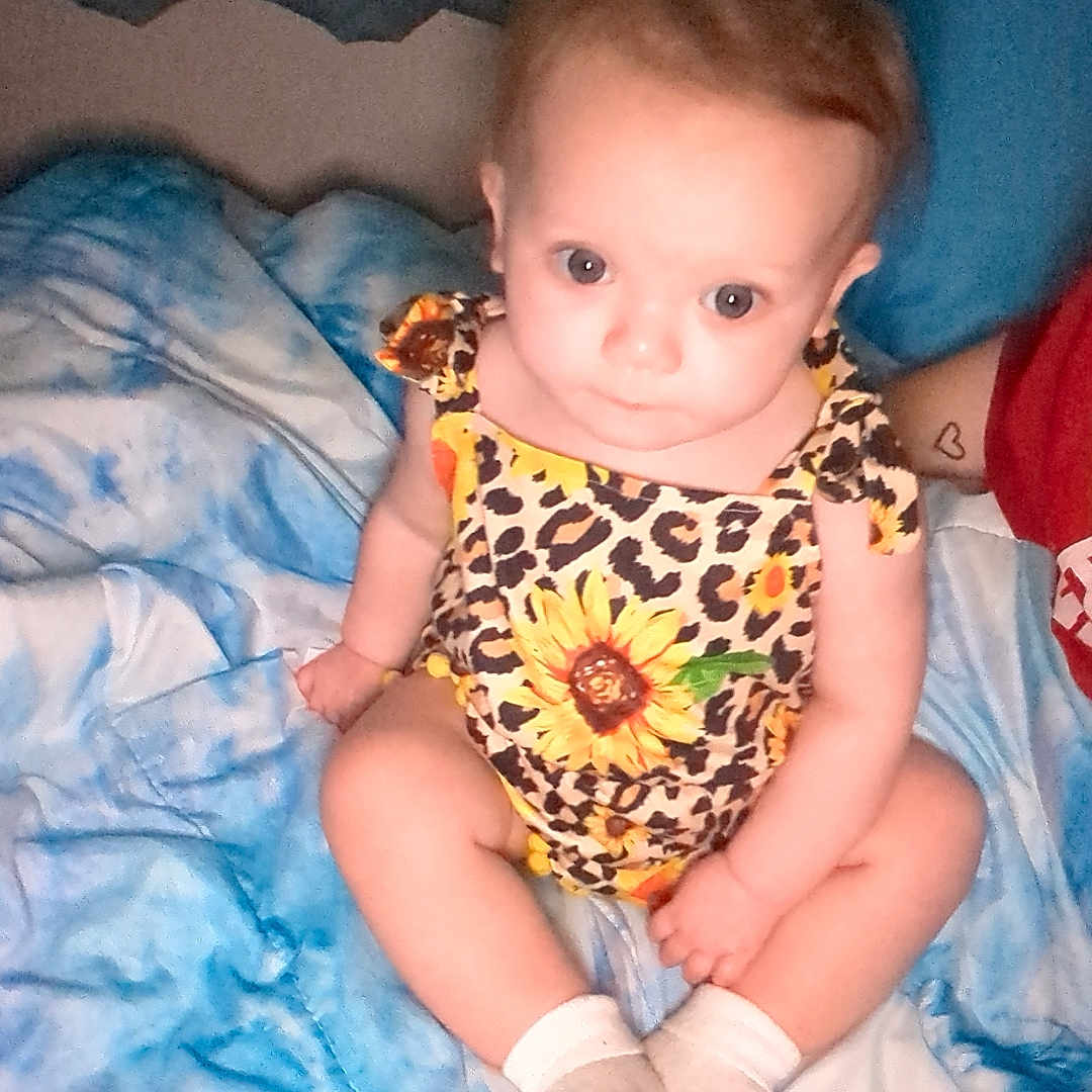 Cristy joined the competition — help win amazing prizes! baby, blanket, blue_blanket, child, closeup, clothing, curious, cute, human, indoor, infant, leopard_print, patterned_clothing, person, portrait, sitting, sunflower_print, tie_dye, white_socks, young_child