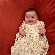 Emy participe au concours pour gagner de l'argent avec cette photo : baby, infant, smile, tongue_out, dress, floral_pattern, cute, chubby_cheeks, sitting, blanket, cozy, child, portrait, happy, indoors, person, young_child, soft_texture, warm_colors, playful