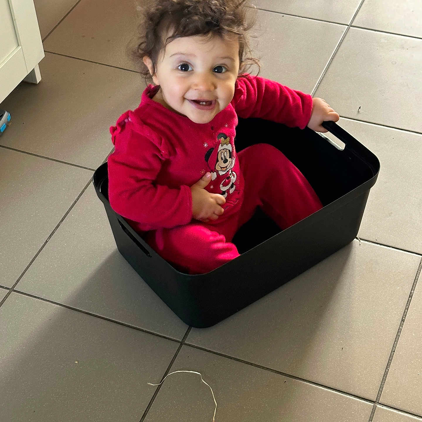Eya a rejoint le concours — aidez-le/la à gagner de superbes lots ! toddler, child, smiling, curly_hair, red_clothing, minnie_mouse, storage_bin, indoor, tile_floor, happy, sitting, person, cute, playful, baby, home, plastic_container, floor, fun, young_child