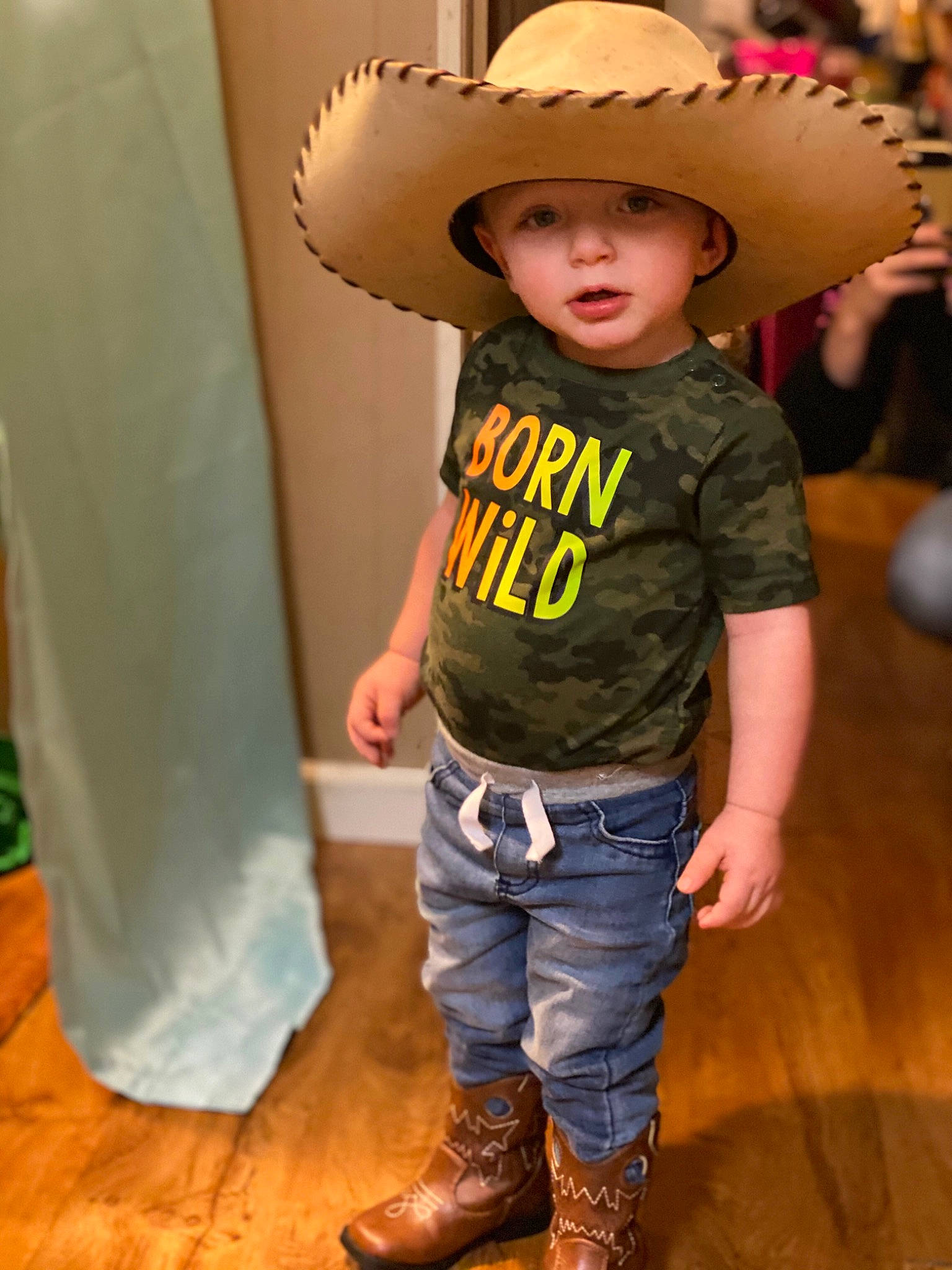 Tucker is registered to the contest to win money with this photo: chin, cool, cowboy_hat, eye, floor, flooring, happy, hat, head, headgear, headwear, human_body, person, shoe, skin, sleeve, sombrero, standing, sun_hat, toddler