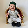 Lynao a rejoint le concours — aidez-le/la à gagner de superbes lots ! baby, child, smile, green_cap, gold_chain, miniature_throne, red_throne, gold_detail, white_background, sitting, casual_clothing, black_shoes, playful, portrait, cute, happy, indoor, fashion, young_child, one_person