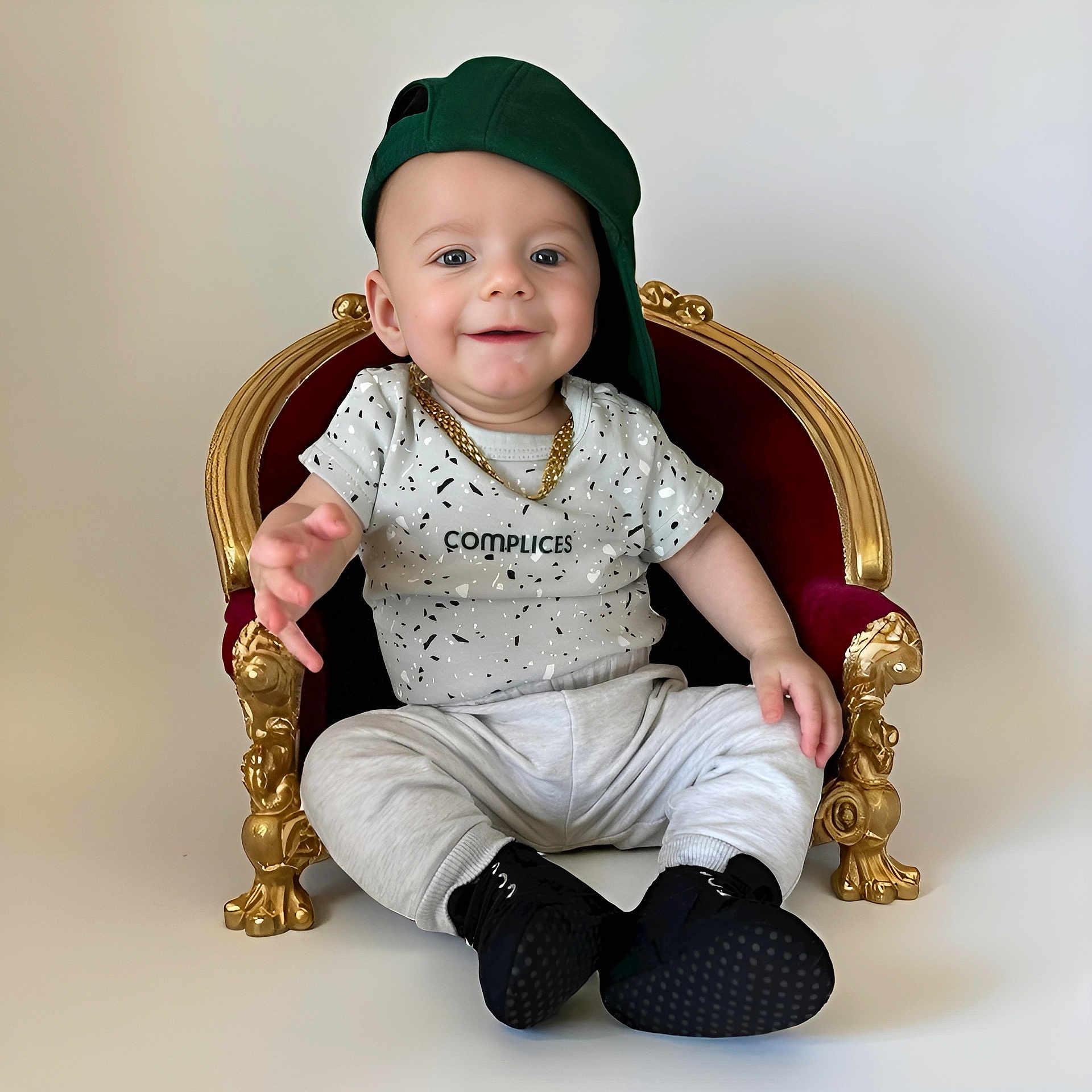 Lynao a rejoint le concours — aidez-le/la à gagner de superbes lots ! baby, black_shoes, casual_clothing, child, cute, fashion, gold_chain, gold_detail, green_cap, happy, indoor, miniature_throne, one_person, playful, portrait, red_throne, sitting, smile, white_background, young_child