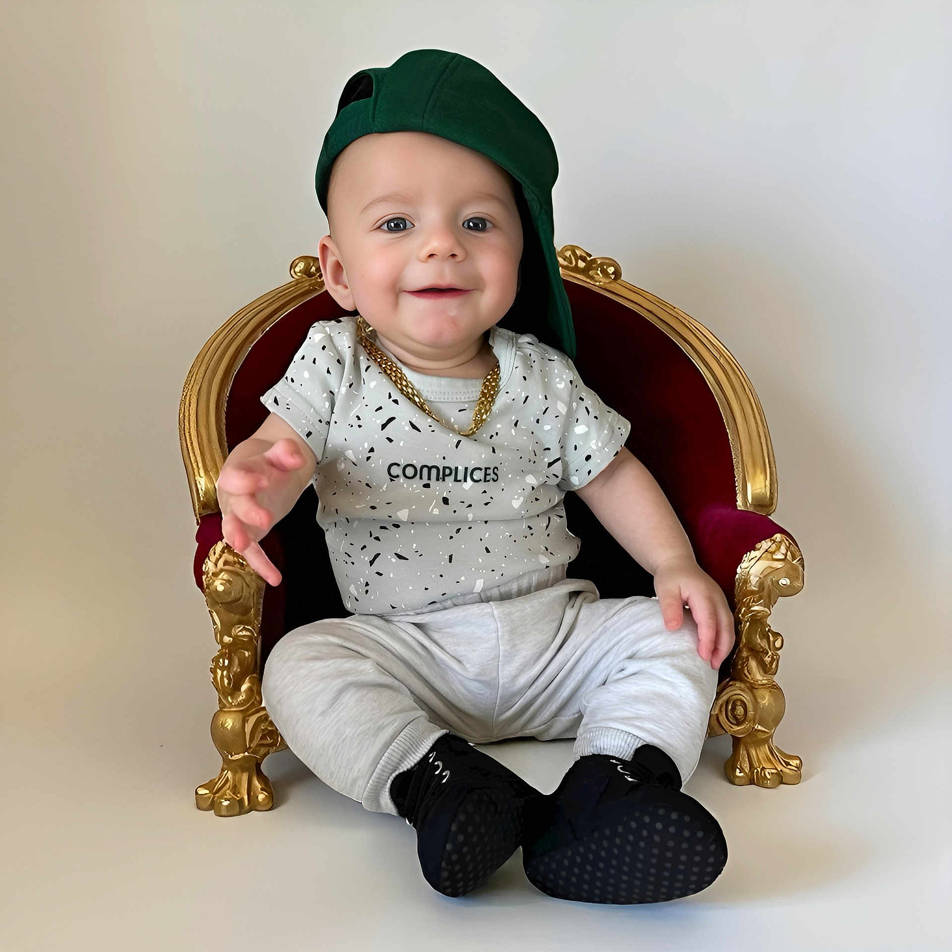 Lynao a rejoint le concours — aidez-le/la à gagner de superbes lots ! baby, child, smile, green_cap, gold_chain, miniature_throne, red_throne, gold_detail, white_background, sitting, casual_clothing, black_shoes, playful, portrait, cute, happy, indoor, fashion, young_child, one_person