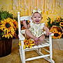 baby, child, smiling, rocking_chair, sunflower, headband, dress, flower, yellow, indoor, happy, cute, portrait, wooden_chair, floor_rug, decor, infant, seated, background, playful