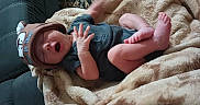 Kashton is registered to the contest to win money with this photo: baby, blanket, hat, yawning, feet, hand, couch, fabric, indoor, infant, clothing, person, sleepy, cute, soft, patterned_rug, relaxing, small, comfortable, toddler