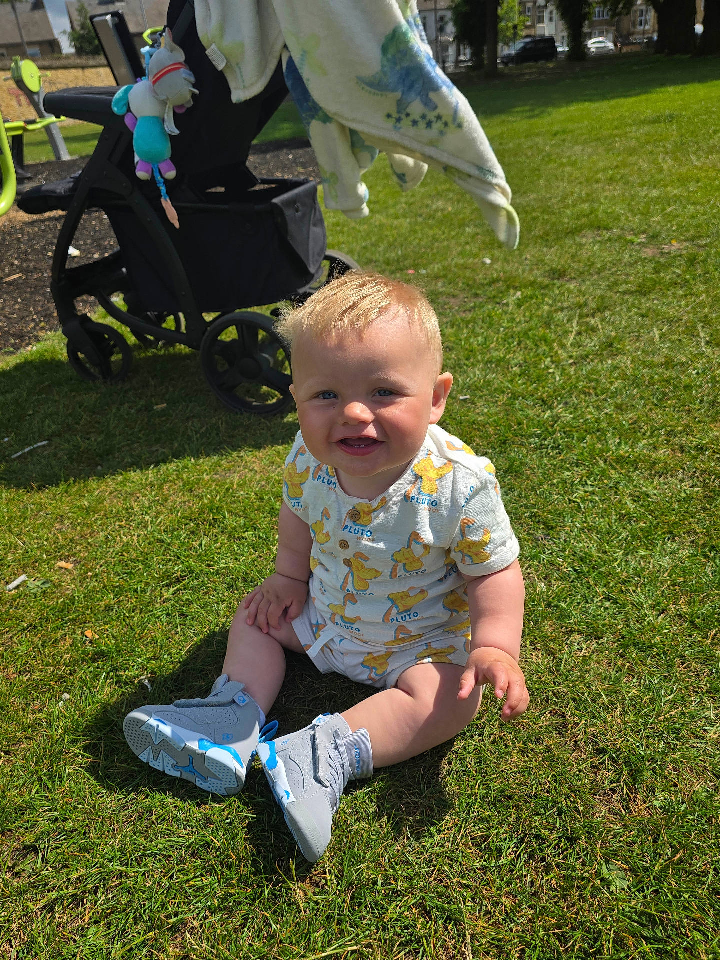 Parker joined the competition — help win amazing prizes! baby, blanket, child, clothing, daytime, footwear, grass, happy, outdoor, park, person, playful, pluto, sitting, smile, sneakers, stroller, summer, sunlight, toy