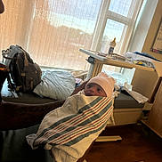 Dior is registered to the contest to win money with this photo: newborn, baby, hospital, blanket, hat, person, arms, tattoo, bottle, table, window, curtain, bed, clothes, indoor, care, infant, wrapped, holding, soft_light