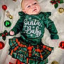 baby, infant, christmas, holiday, ornaments, green_clothing, plaid_skirt, headband, red_socks, blanket, festive, cute, lying_down, soft_texture, decorations, holiday_theme, child, smiling, portrait, celebration