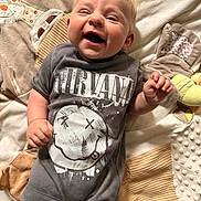 Autumn is registered to the contest to win money with this photo: baby, smiling, laughing, infant, nirvana_tshirt, clothing, blanket, soft_toy, cute, happy, lying_down, child, indoor, face, young_child, toddler, person, apparel, closeup, expression