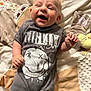 baby, smiling, laughing, infant, nirvana_tshirt, clothing, blanket, soft_toy, cute, happy, lying_down, child, indoor, face, young_child, toddler, person, apparel, closeup, expression