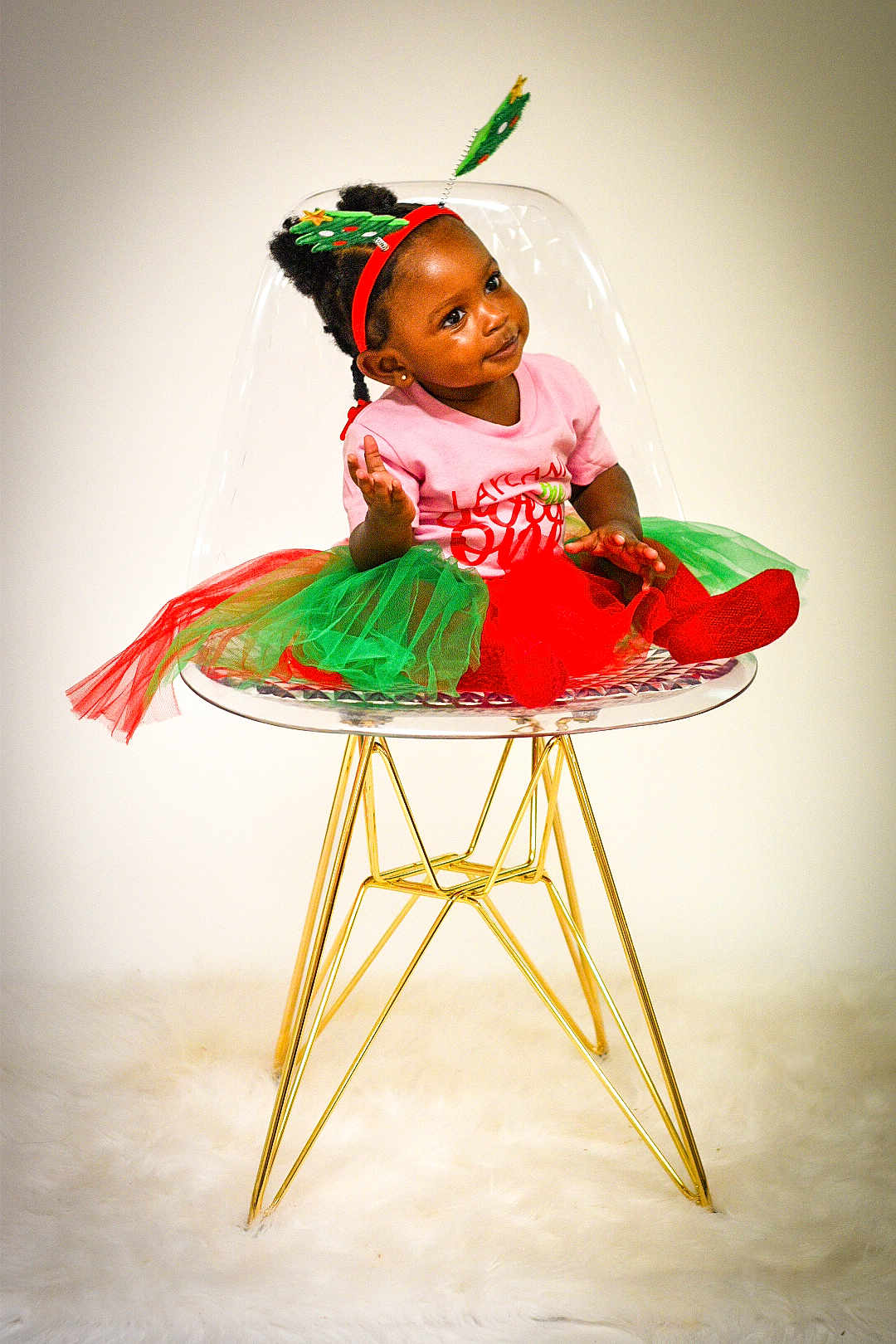 Laylani joined the competition — help win amazing prizes! toddler, child, chair, transparent_chair, golden_legs, tutu, red_socks, pink_shirt, headband, christmas_tree_headband, holiday, indoor, portrait, cute, smile, curious, fluffy_rug, modern_furniture, fashion, celebration