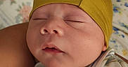 Christian is registered to the contest to win money with this photo: baby, bed, caregiver, close_up, closed_eyes, cozy, face, floral_blanket, indoors, infant, knit_cap, newborn, onesie, peaceful, photography, portrait, resting, sleeping, striped_clothing, yellow_hat