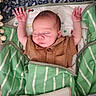 Christian is registered to the contest to win money with this photo: newborn, baby, sleeping, infant, child, portrait, crib, blanket, green_blanket, striped_blanket, brown_clothing, raised_arms, peaceful, indoors, bed, floral_pattern, face, closed_eyes, cozy, photography