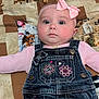 baby, infant, pink_bow, denim_overalls, embroidered_flowers, patchwork_quilt, animal_print, cat_print, dog_print, lying_down, cute, child, face, headband, clothing, portrait, indoor, chubby_cheeks, curious_expression, soft_lighting
