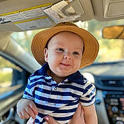Say is registered to the contest to win money with this photo: baby, child, hat, striped_shirt, blue, white, smiling, indoors, car_interior, person, hands, cute, portrait, young, headwear, casual_clothing, seatbelt, window, daylight, happy