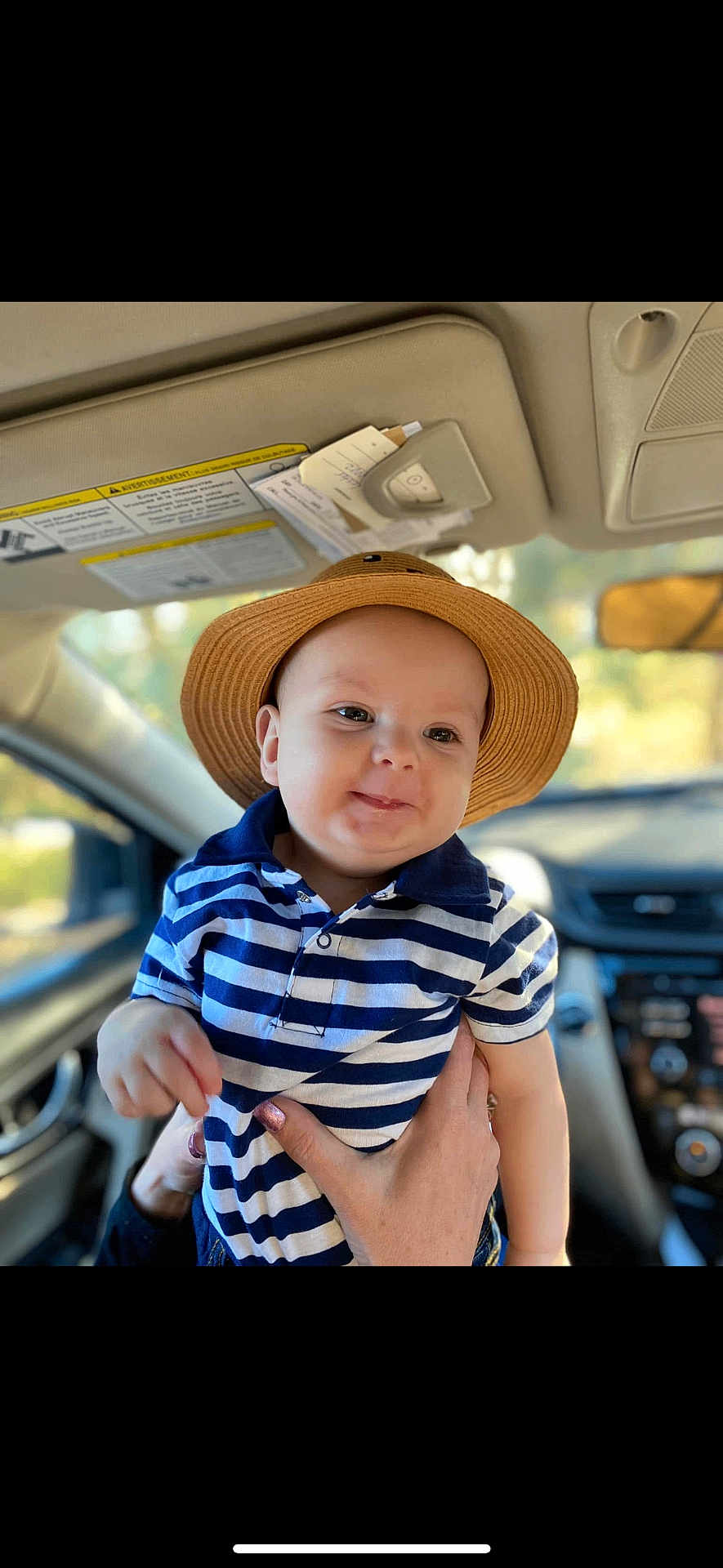 Say is registered to the contest to win money with this photo: baby, child, hat, striped_shirt, blue, white, smiling, indoors, car_interior, person, hands, cute, portrait, young, headwear, casual_clothing, seatbelt, window, daylight, happy
