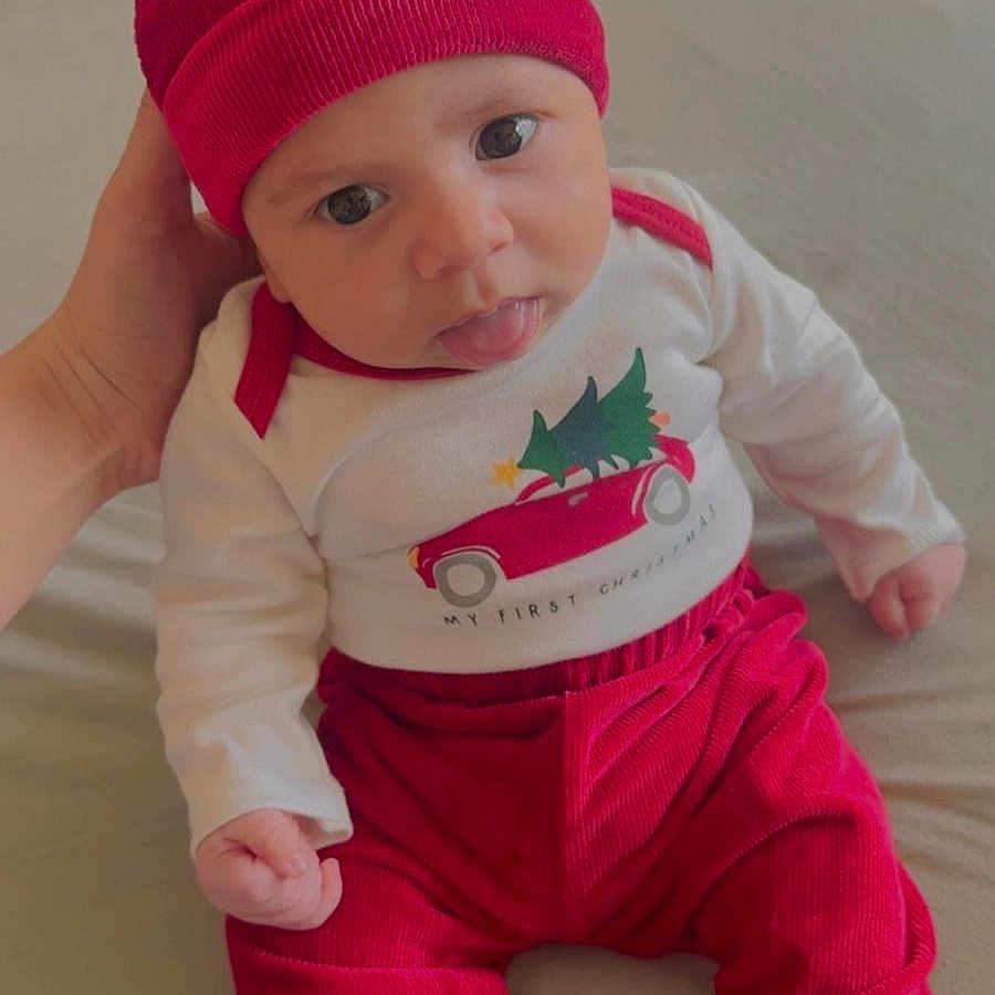 Yazeed joined the competition — help win amazing prizes! baby, infant, child, red_clothing, hat, tongue_out, cute, hand, sitting, indoors, soft_surface, playful, festive, long_sleeve_shirt, pants, person, portrait, young_child, cozy, expression