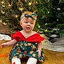 baby, bow, child, christmas_tree, cute, decorations, festive_clothing, floor, greenery, happy, headband, holiday, indoors, lights, red_shoes, seasonal, sitting, smiling, toddler, wooden_floor