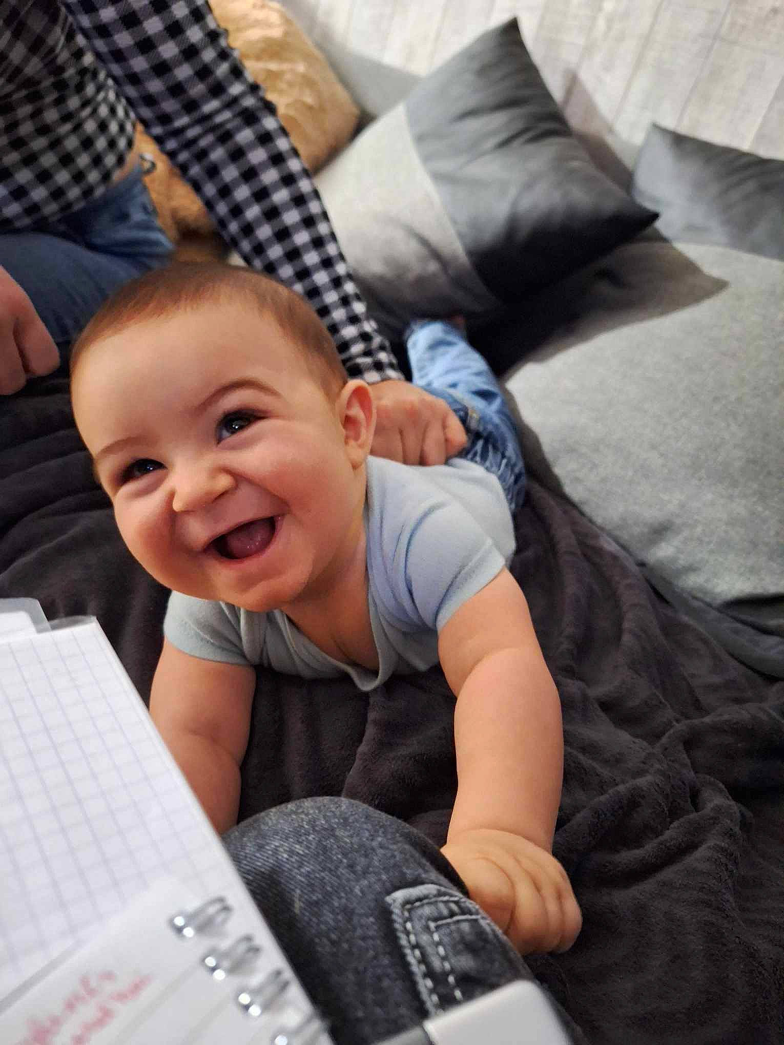 Kendji a rejoint le concours — aidez-le/la à gagner de superbes lots ! baby, baby_products, baby_toddler_clothing, bedding, child, comfort, finger, fun, happy, joy, lap, laugh, linens, pattern, person, pillow, room, sitting, smile, t_shirt