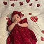 baby, infant, red_dress, headband, heart, lollipop, blanket, cute, decorations, lying_down, indoors, portrait, adorable, hands, face, child, soft_texture, valentine, festive, holiday